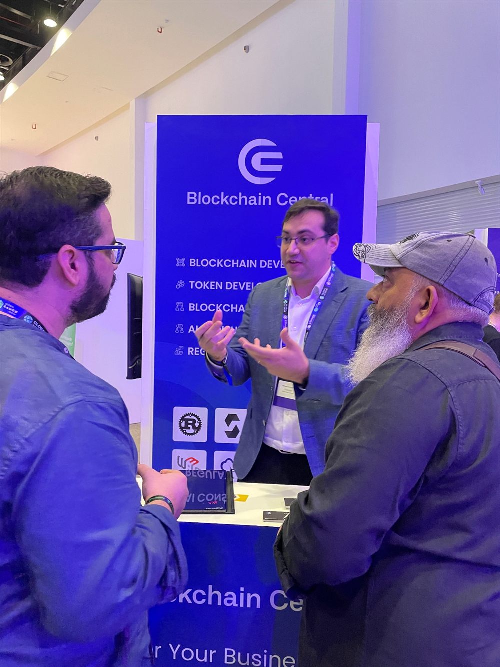 Blockchain Central representative speaking with visitors at a conference booth.